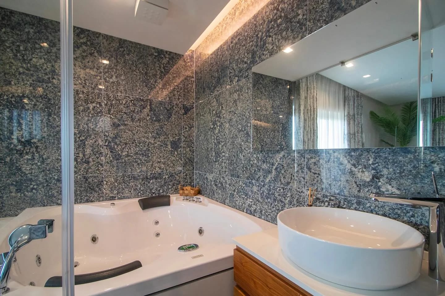 Bathroom clad in speckled granite with a corner whirlpool bath and a vessel basin on a wood vanity