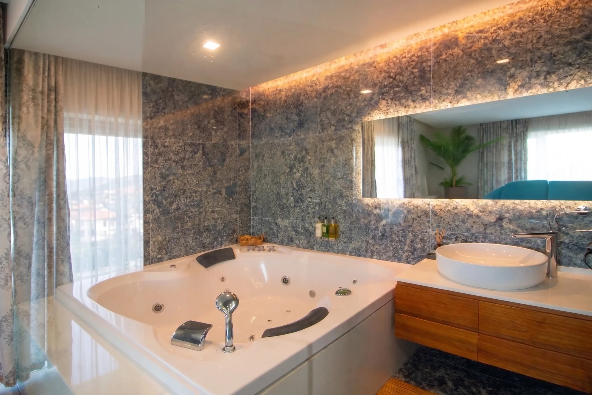 Corner whirlpool bath with jets, headrests and a digital control panel against grey stone tiling