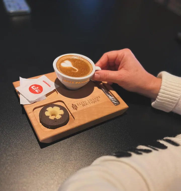 Hand holding cappuccino cup on branded wooden board with biscuit