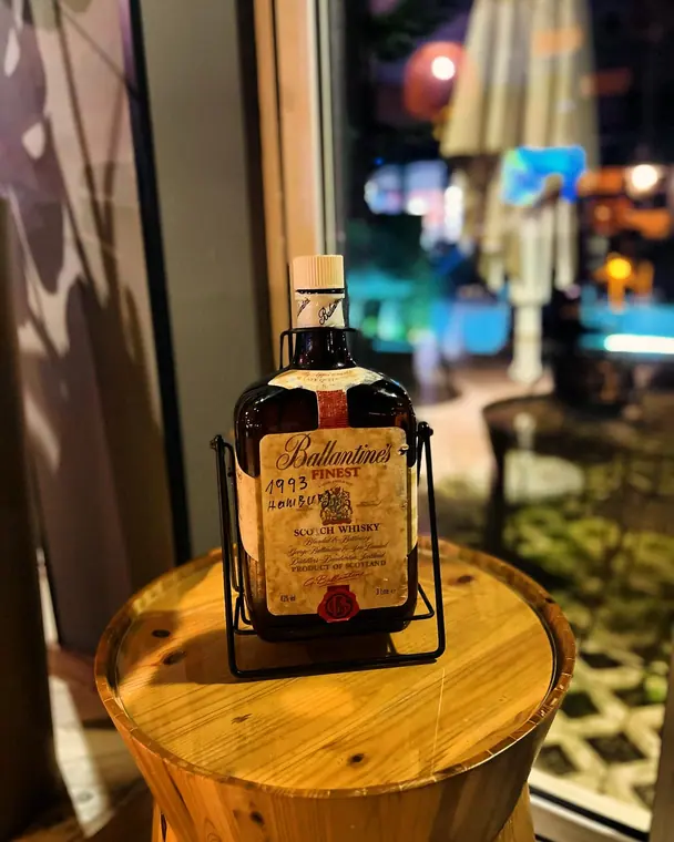 Large whisky bottle in metal cradle on wooden barrel top