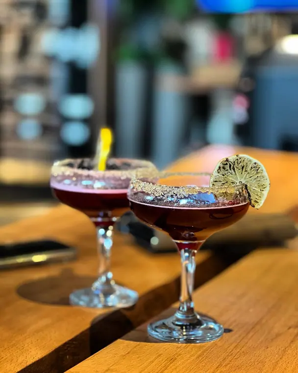 Two sugar-rimmed cocktails with dried lime on a wooden bar counter