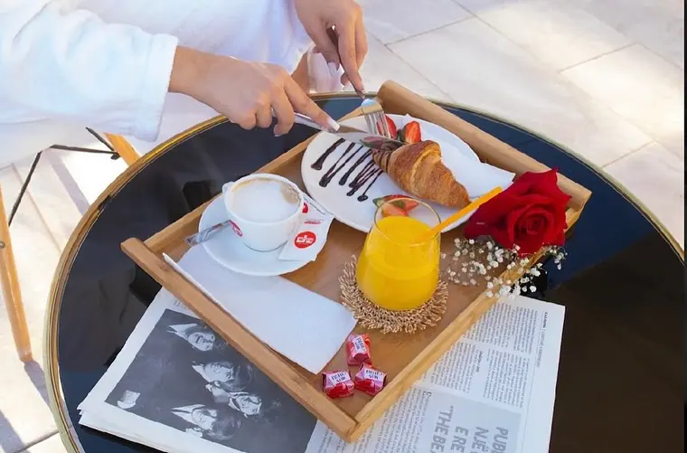 Breakfast tray with croissant, cappuccino, juice and rose on glass table