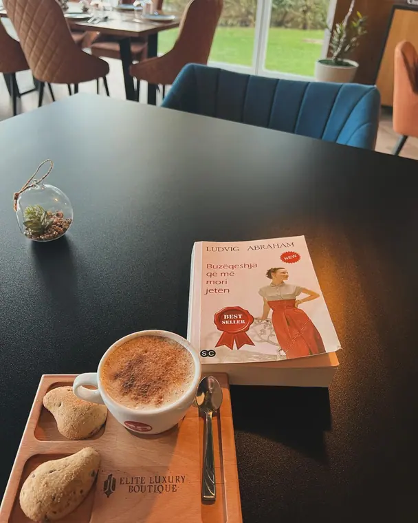 Cappuccino and biscuits on wooden tray beside a paperback book