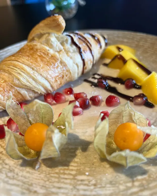 Close view of croissant with pomegranate seeds, physalis and mango