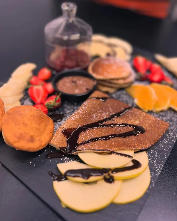 Crepe with chocolate sauce, pancakes, fruit and spread on slate