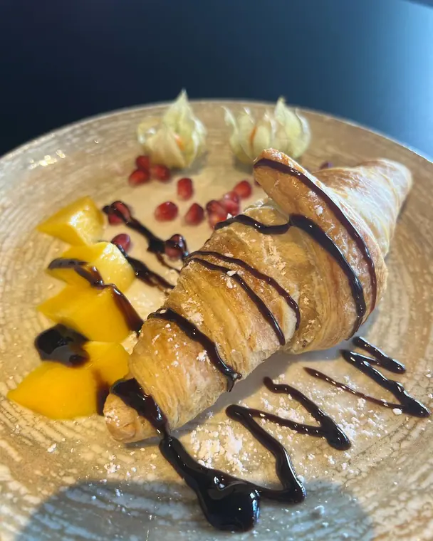 Croissant with chocolate sauce, mango and pomegranate on ceramic plate