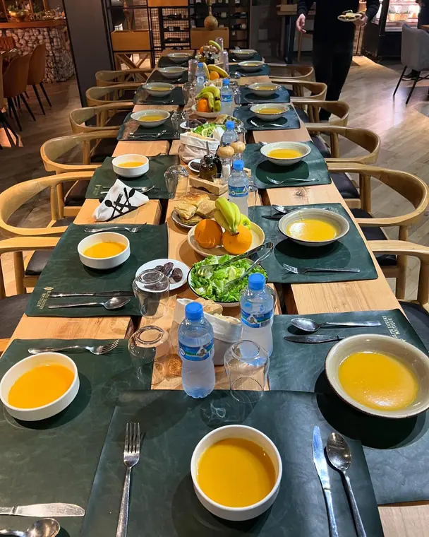 Long table set with soup bowls, bread, fruit and water bottles