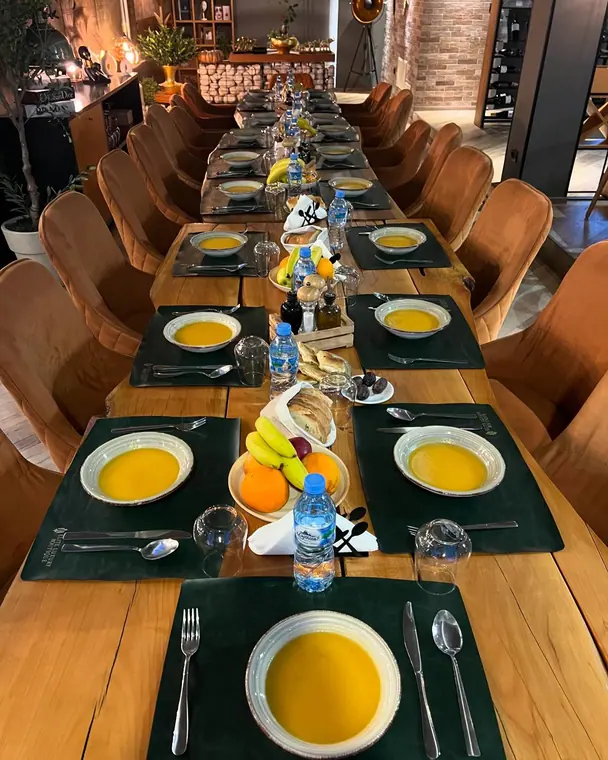 Long wooden table with soup bowls and fruit, orange velvet chairs