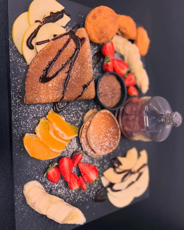 Overhead slate board with crepe, pancakes, fruit and jam jar