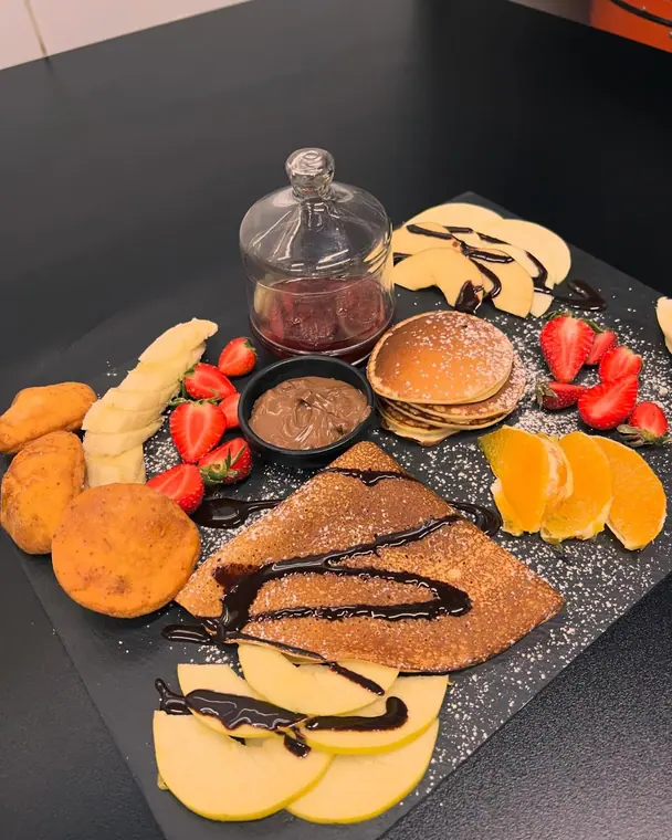 Slate board of crepe, pancakes, fritters and sliced fruit