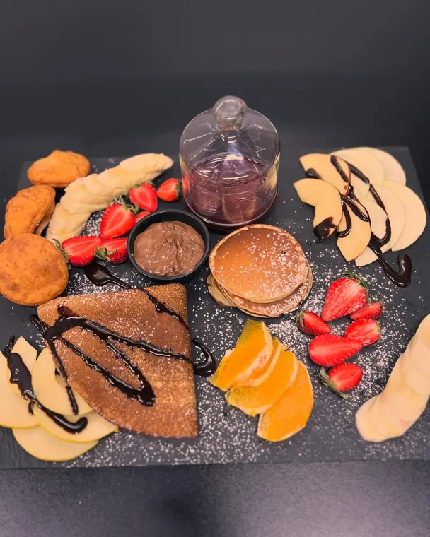 Slate board with crepe, pancakes, fritters, fruit and spread