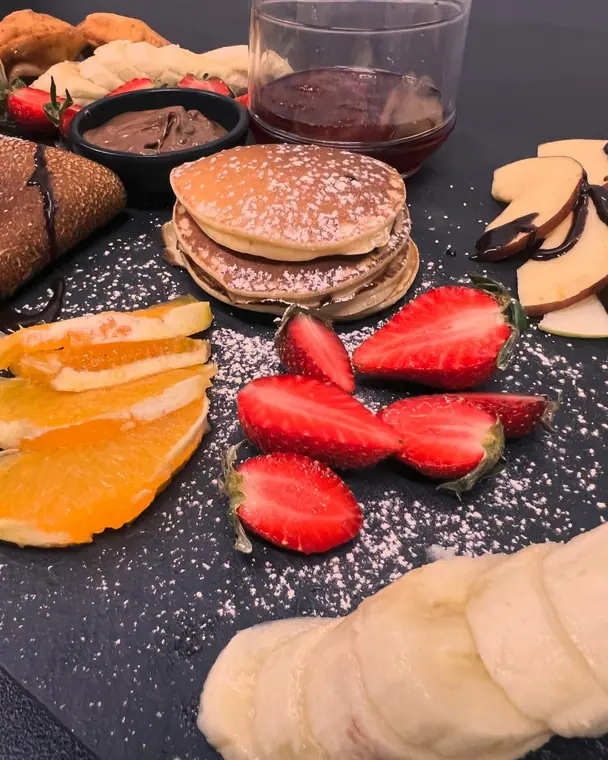 Slate board with pancakes, sliced fruit, chocolate spread and jam
