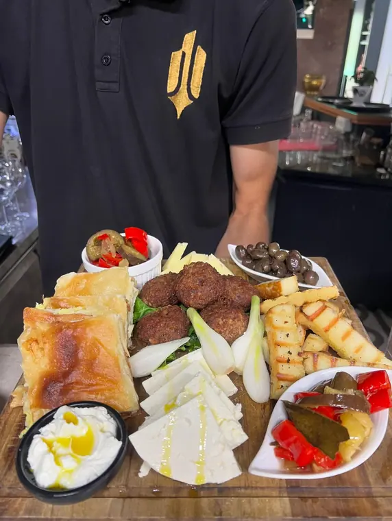 Staff member holds a breakfast board with cheese and byrek
