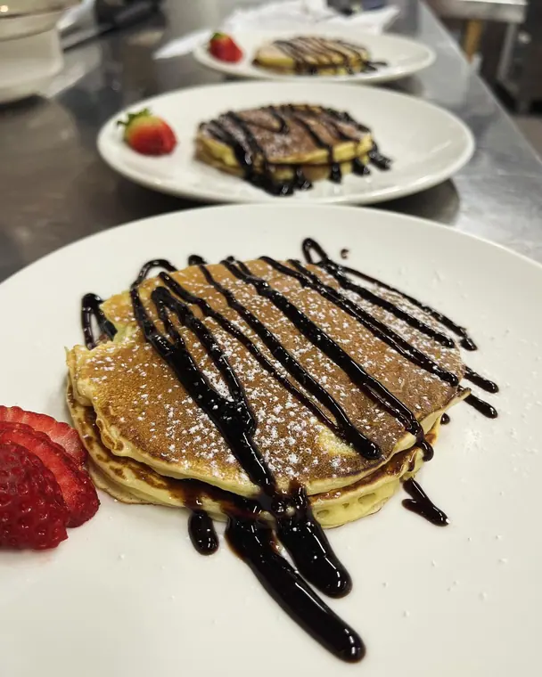 Three plates of pancakes with chocolate sauce and strawberries
