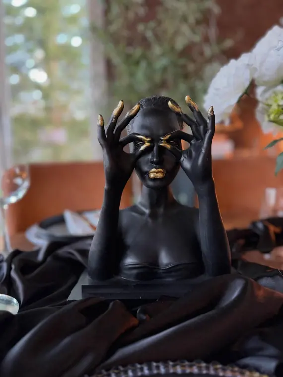 Black and gold figurine bust on dressed table with satin runner