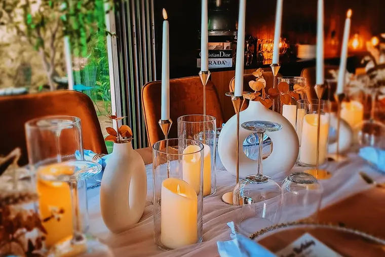 Candles and ceramic vases on table, shelf of designer boxes behind
