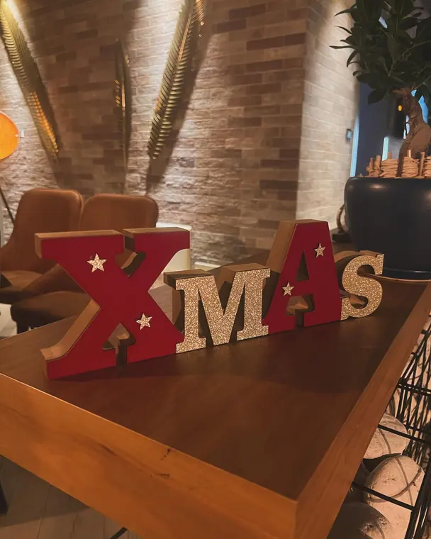 Freestanding XMAS letter ornament on wooden table by brick wall