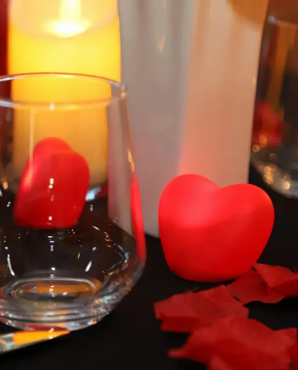 Red heart ornaments beside glass tumblers and pillar candle