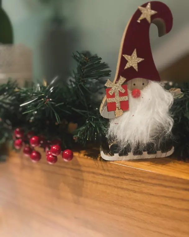 Wooden gnome figure with red hat on shelf beside pine garland