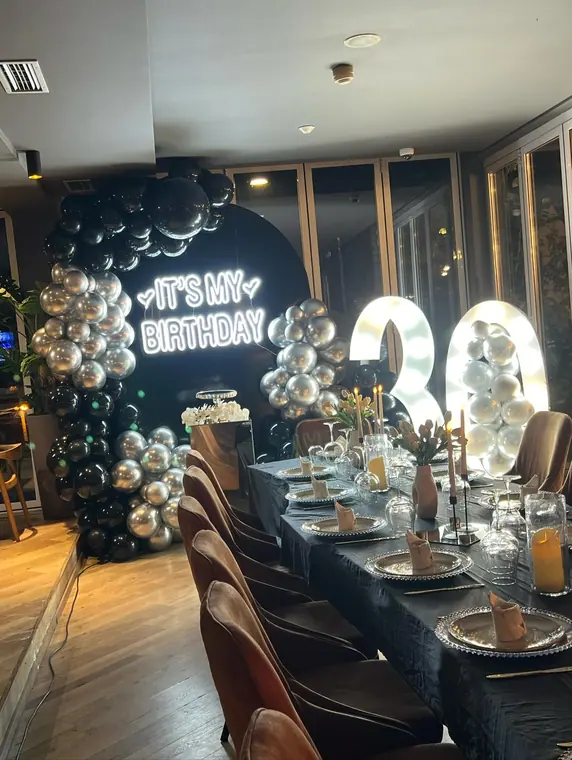 Balloon arch, neon sign and set table in restaurant interior