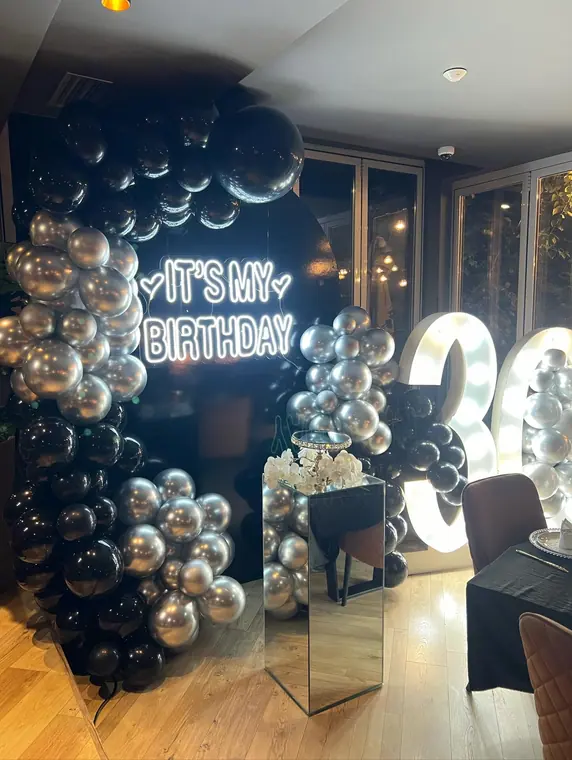 Black and silver balloon arch with neon sign and lit number 30