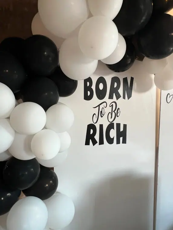Black and white balloon arch beside board lettered Born To Be Rich