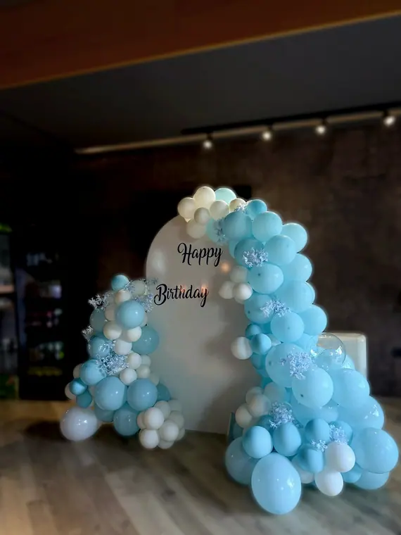 Blue and white balloon arch around Happy Birthday board indoors