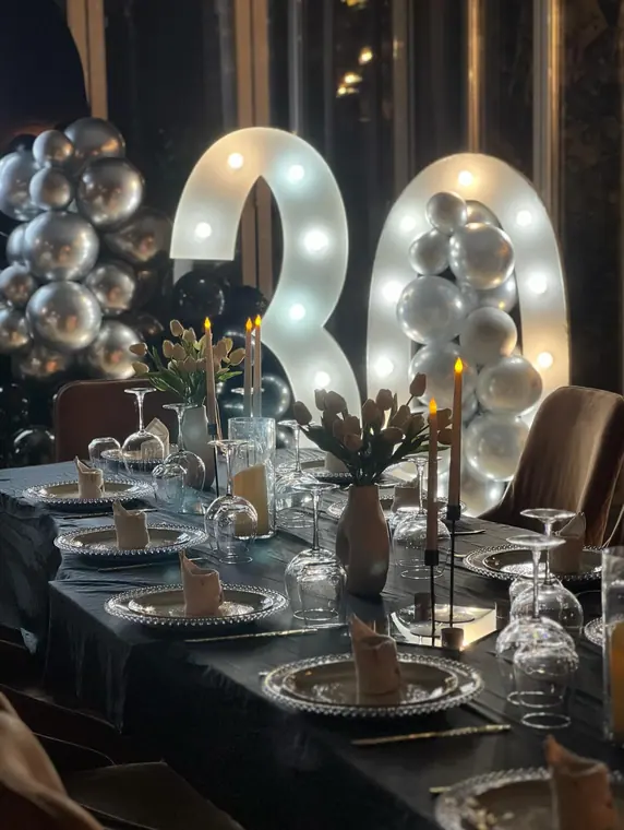Lit number 30 and silver balloons behind set table with candles