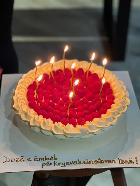 Raspberry cream cake with lit candles and Albanian icing message