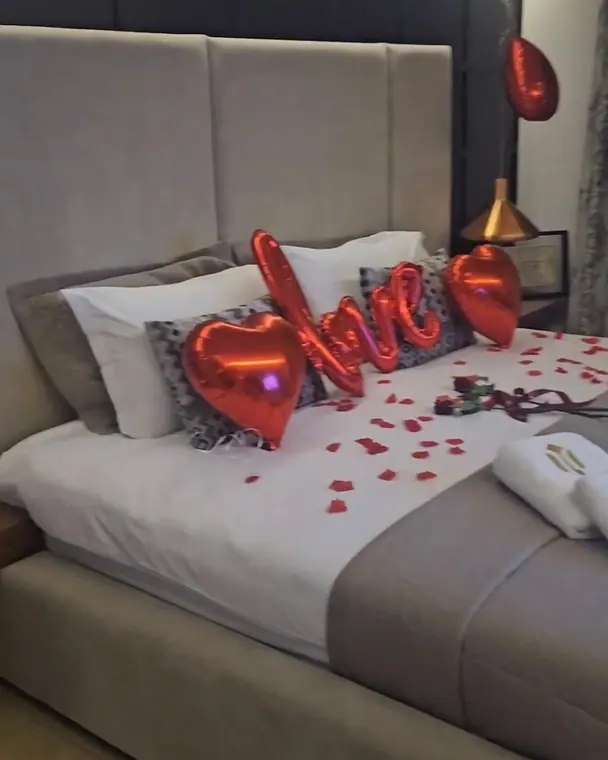 Bed dressed with heart balloons, rose petals and robe