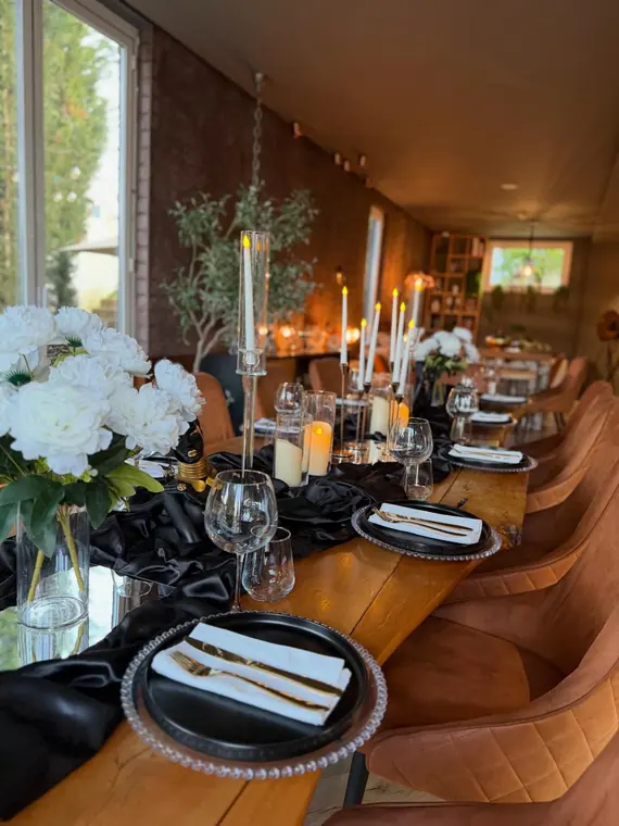Long table with black runner, gold cutlery, candles and white flowers