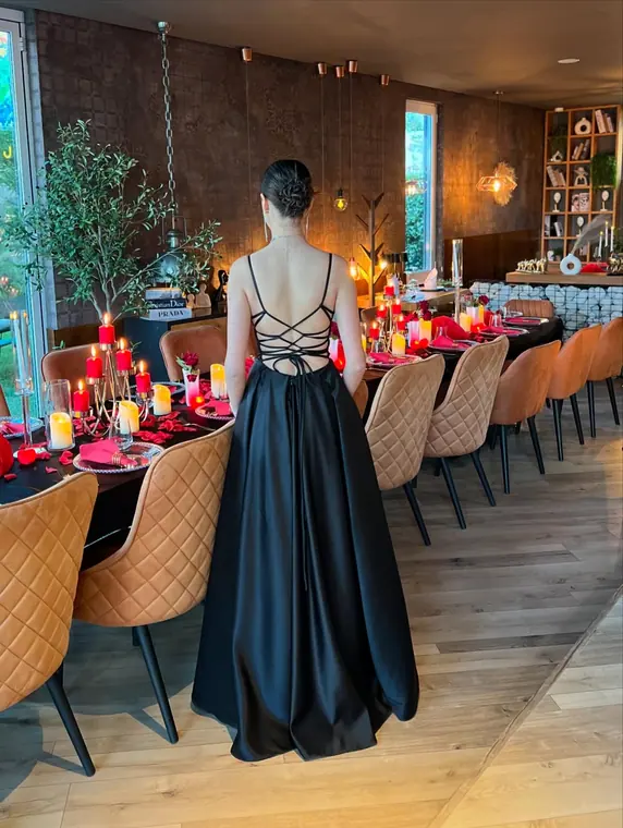 Woman in black gown facing banquet table with red candles and rose petals