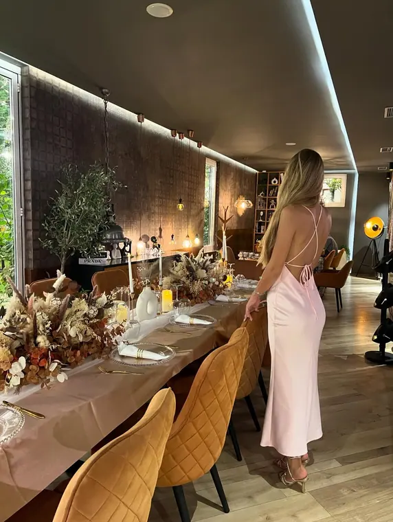 Woman in pink dress beside table with dried floral runner and candles