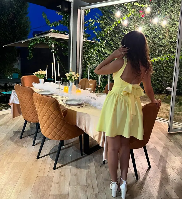 Woman in yellow dress seen from behind at a set dining table