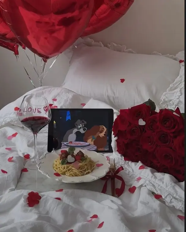 Bed picnic with spaghetti, wine, roses and a tablet playing a film