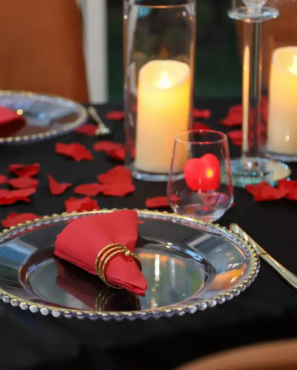 Glass charger with red napkin, pillar candles and scattered petals