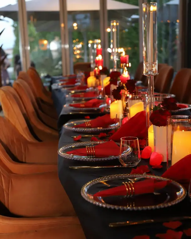 Long black-clothed table with red napkins, roses and candles