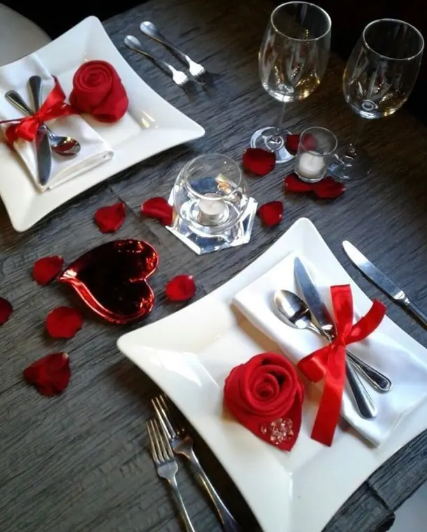 Two place settings with rose-folded napkins, candles and petals