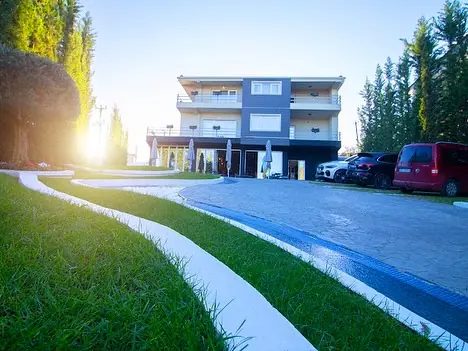 Three-storey hotel building at sunset with lawn, path and parked cars
