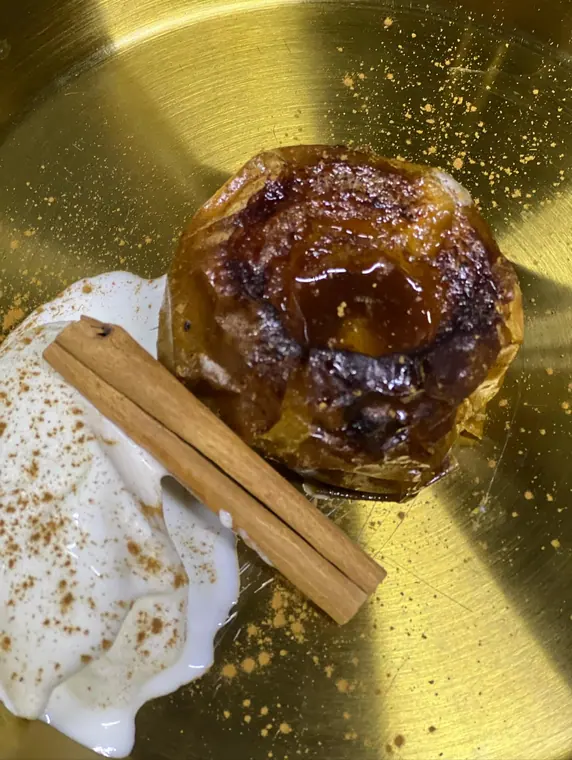Baked apple with cream and cinnamon stick on gold plate