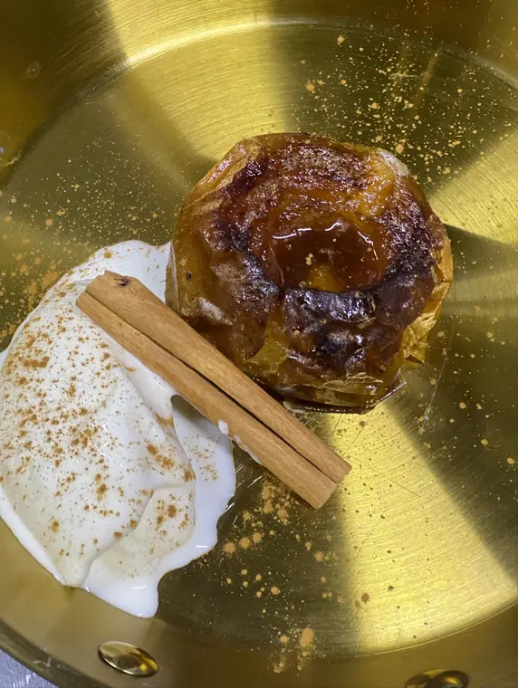 Baked apple with cream and cinnamon stick on gold plate