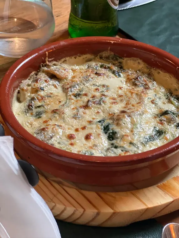 Baked cheese and spinach dish in terracotta dish on wooden board
