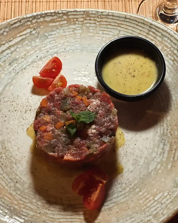 Beef tartare disc with cherry tomatoes and sauce in a ceramic bowl