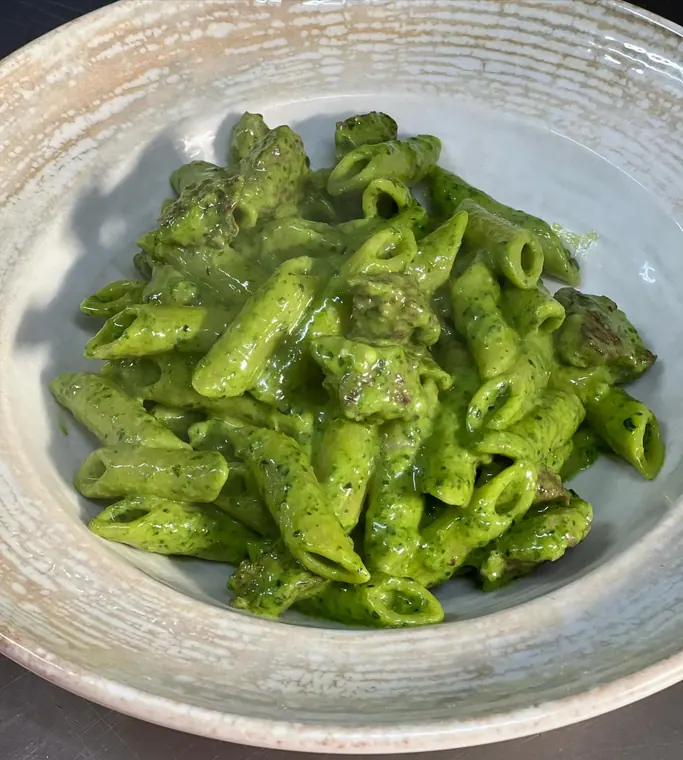 Bowl of penne in bright green sauce with meat pieces