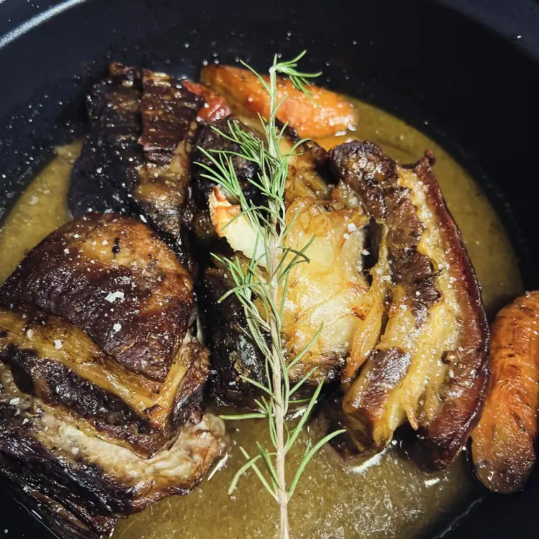 Braised meat pieces with carrot and rosemary in black pan