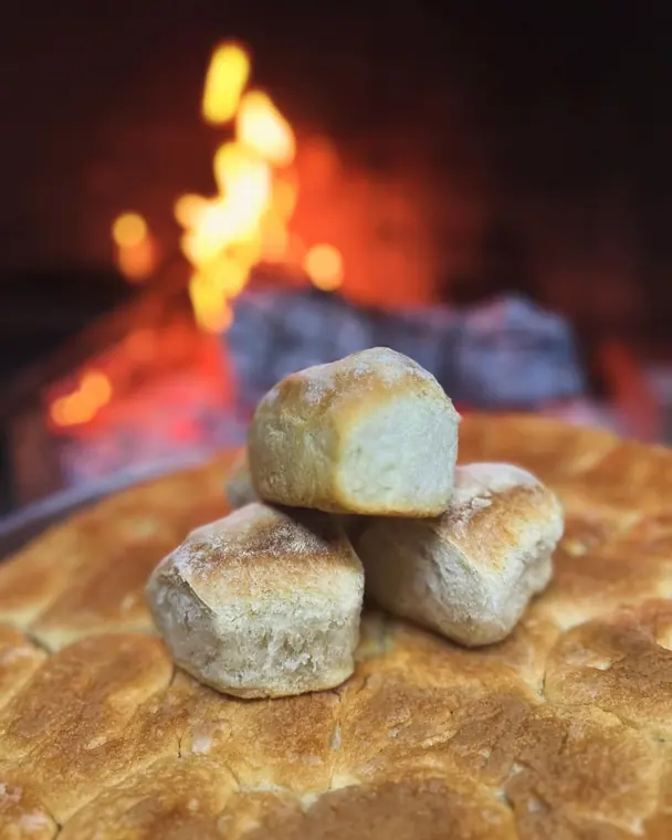 Bread rolls stacked on flatbread in front of an open wood fire
