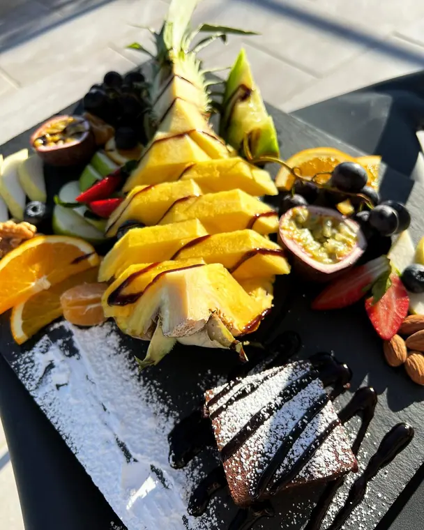 Carved pineapple with mixed fruit and dusted brownie on slate board