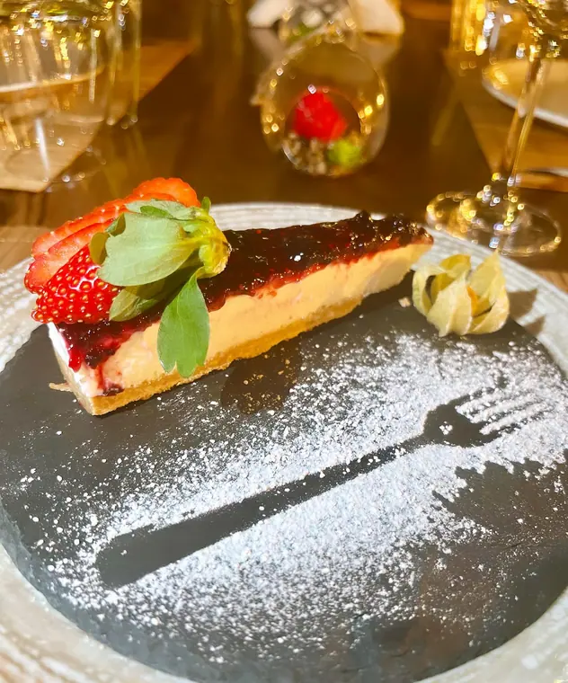 Cheesecake slice with berry topping and strawberry on slate plate