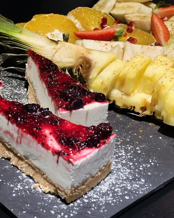 Cheesecake slices with berry topping and sliced fruit on slate