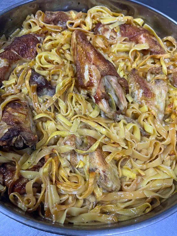 Chicken and noodle dish filling a stainless steel pan